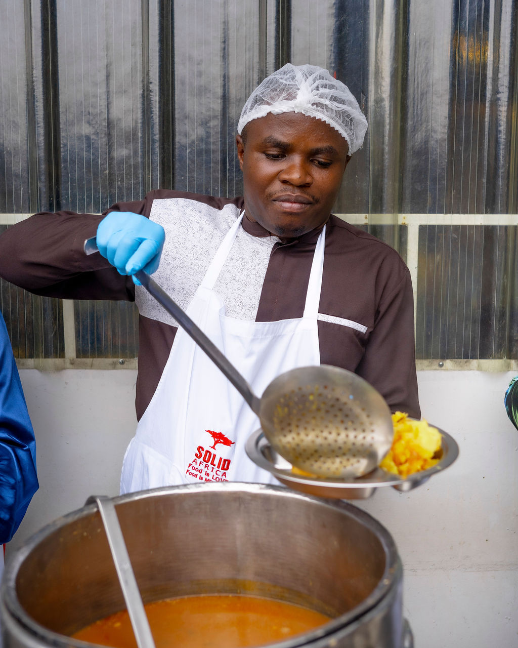 A Solid’Africa cook ladling food from a large pot for the feeding programme